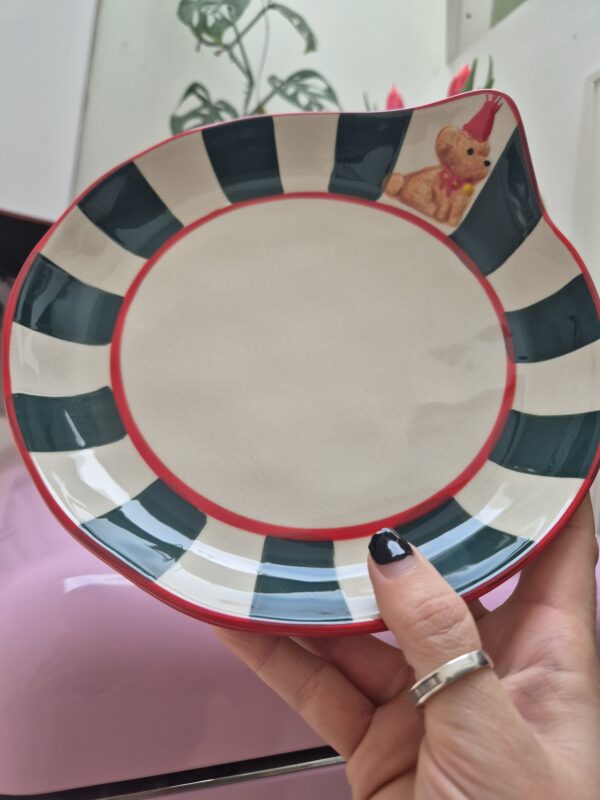 A close-up photo of a handmade ceramic plate with a smooth gloss glaze in soft off-white with Green stripes. The plate has a rounded body, with Red edging and a 3D Brown poodle dog puppy on the front.