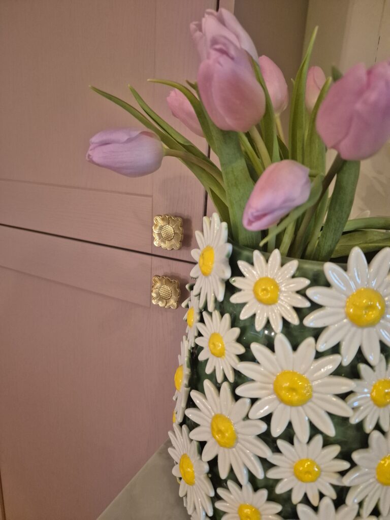 A close-up photo of a handmade ceramic Green vase with a smooth, gloss glaze in soft Green. The natural light casting gentle shadows that highlight its colourway of Red love hearts or Pink love hearts.